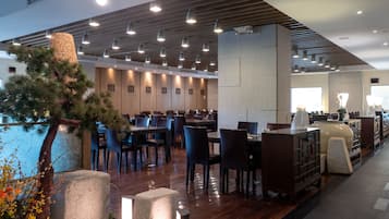 Una hall moderna di un hotel, con pannelli in legno, diverse zone relax e un albero decorativo.