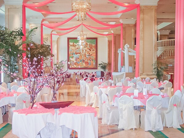 A banquet hall with white tables and chairs, pink drapery, and a chandelier. - Holiday Resort & Spa Guam (Tamuning)