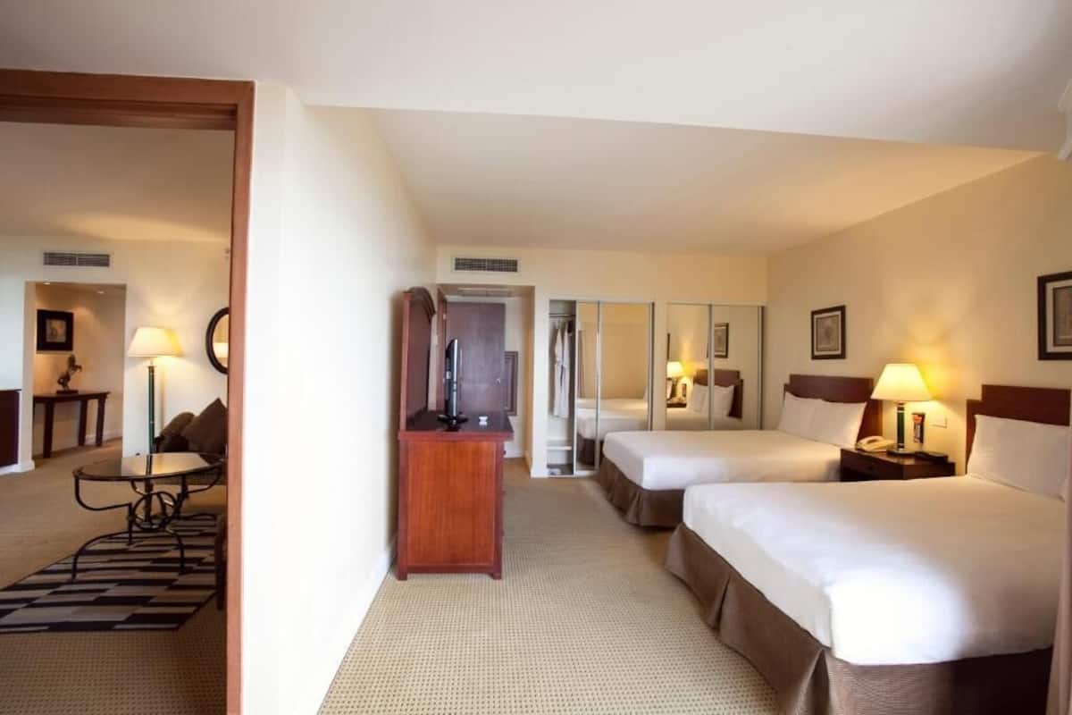 A hotel room with two beds, a desk, a chair, a TV, and a mirror.