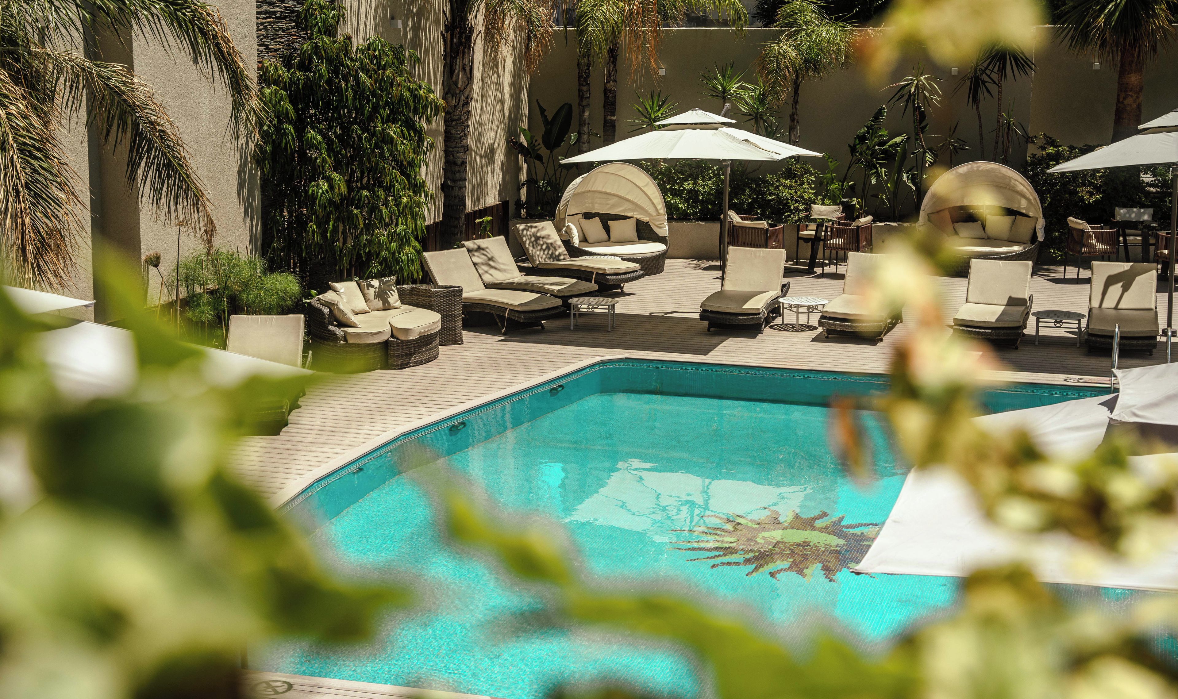 A poolside area with lounge chairs and umbrellas, surrounded by tropical plants.