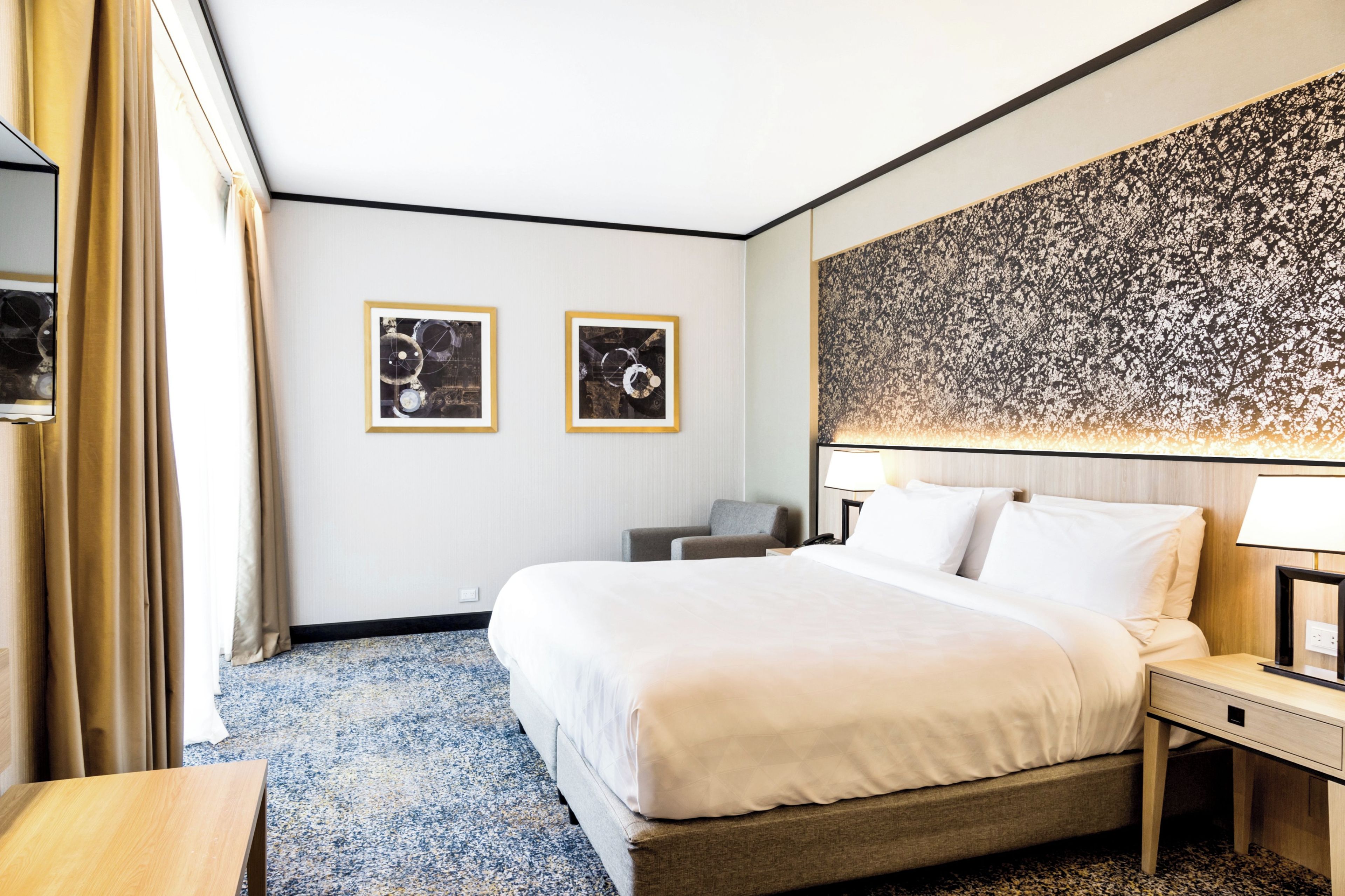 A hotel room with a large bed, a desk, a chair, and two framed pictures on the wall.