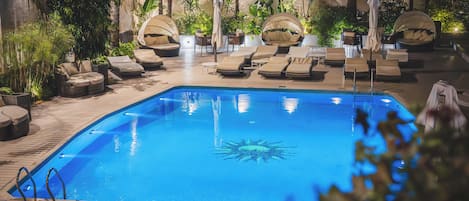 A pool area with lounge chairs and umbrellas, surrounded by tropical plants.