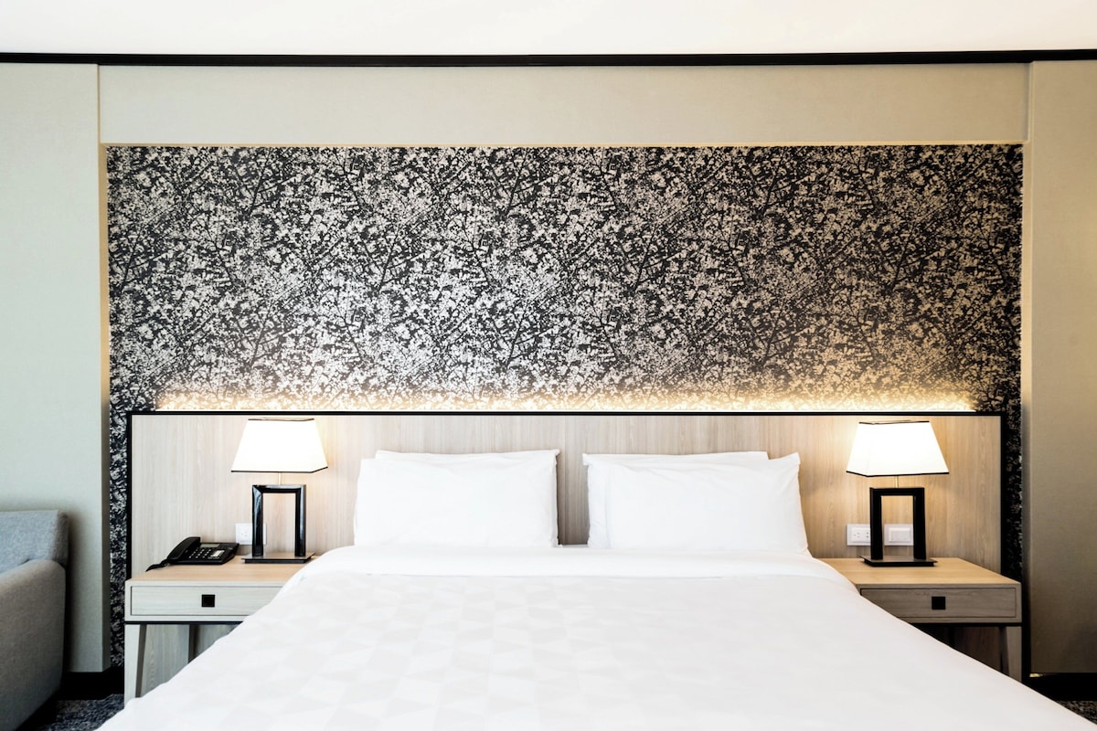 Une chambre d’hôtel avec un grand lit, deux tables de chevet avec des lampes et une tête de lit à motifs floraux.
