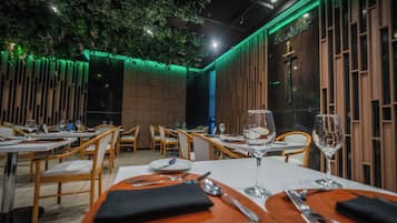 Un restaurante con sillas de madera, mesas dispuestas con cubiertos y una pared iluminada en verde.