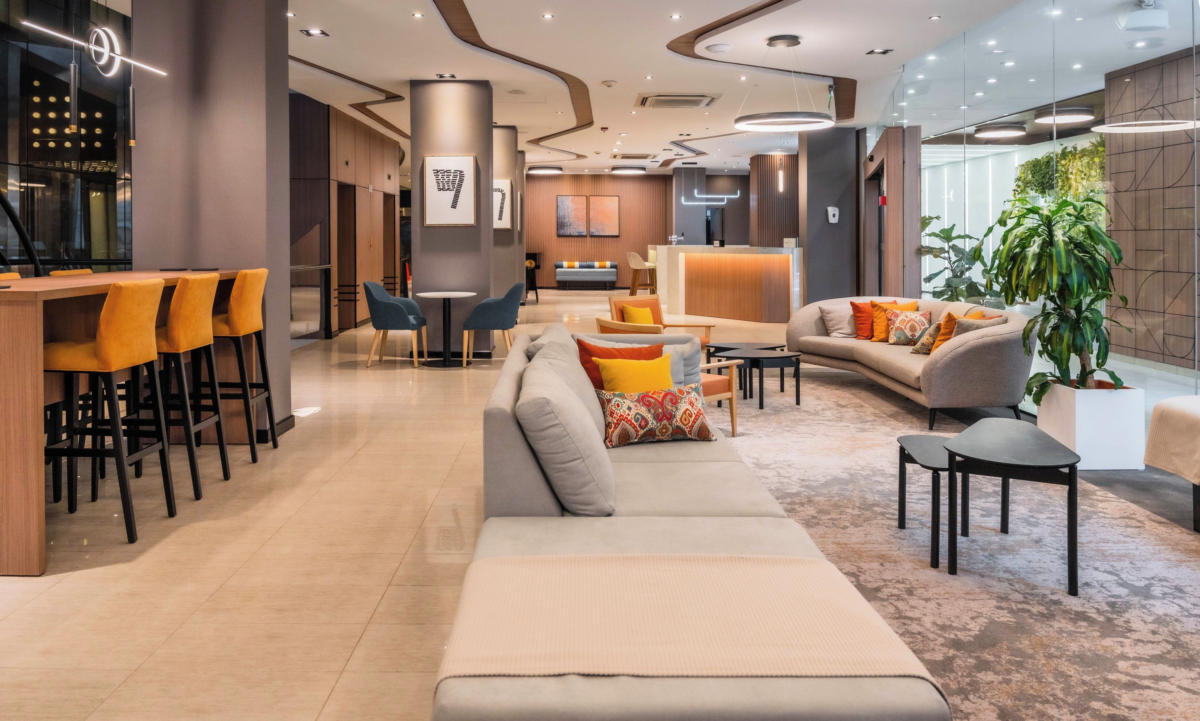 A modern lobby with a reception desk, seating area, and a large plant.