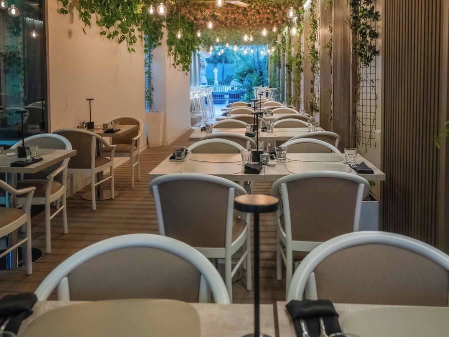 A restaurant with long tables and chairs, hanging lights, and greenery.