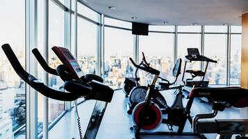 A gym with stationary bikes and a treadmill, large windows with a city view, and a curved ceiling.