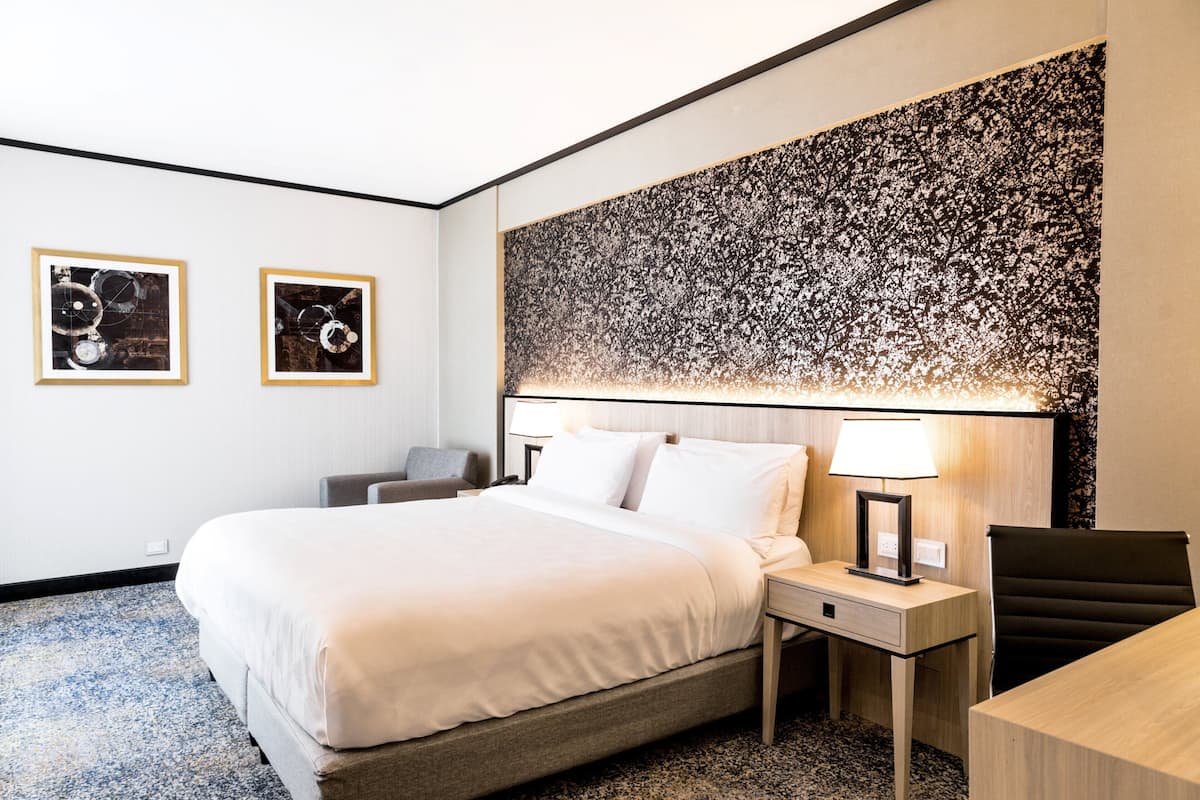 A hotel room with a large bed, a desk, a chair, two bedside tables, and two framed pictures on the wall.