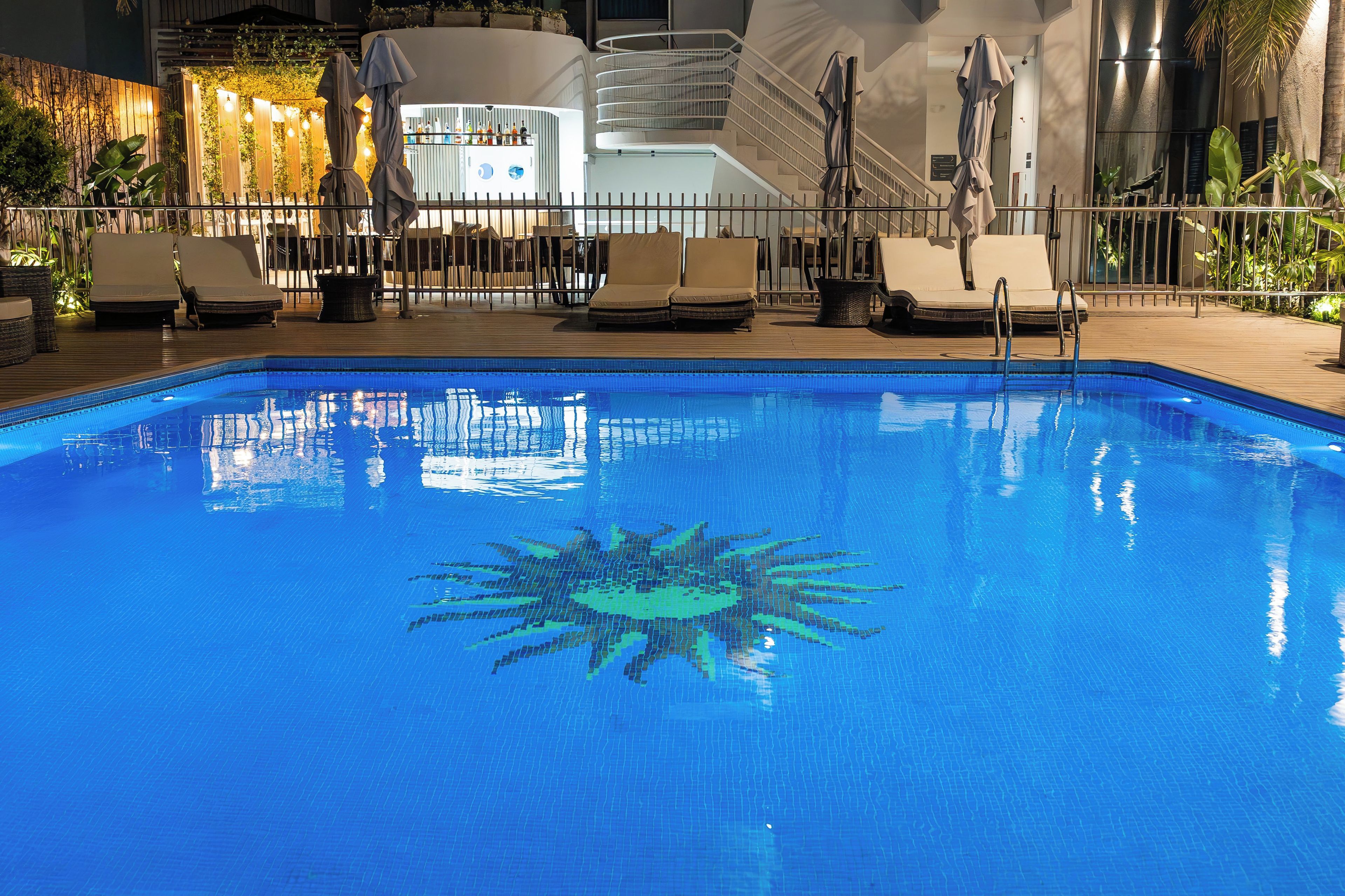 Ein Swimmingpool mit Sonnendesign, umgeben von Liegestühlen und einer Bar.