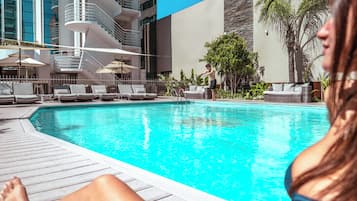 A swimming pool with lounge chairs and a modern building in the background.
