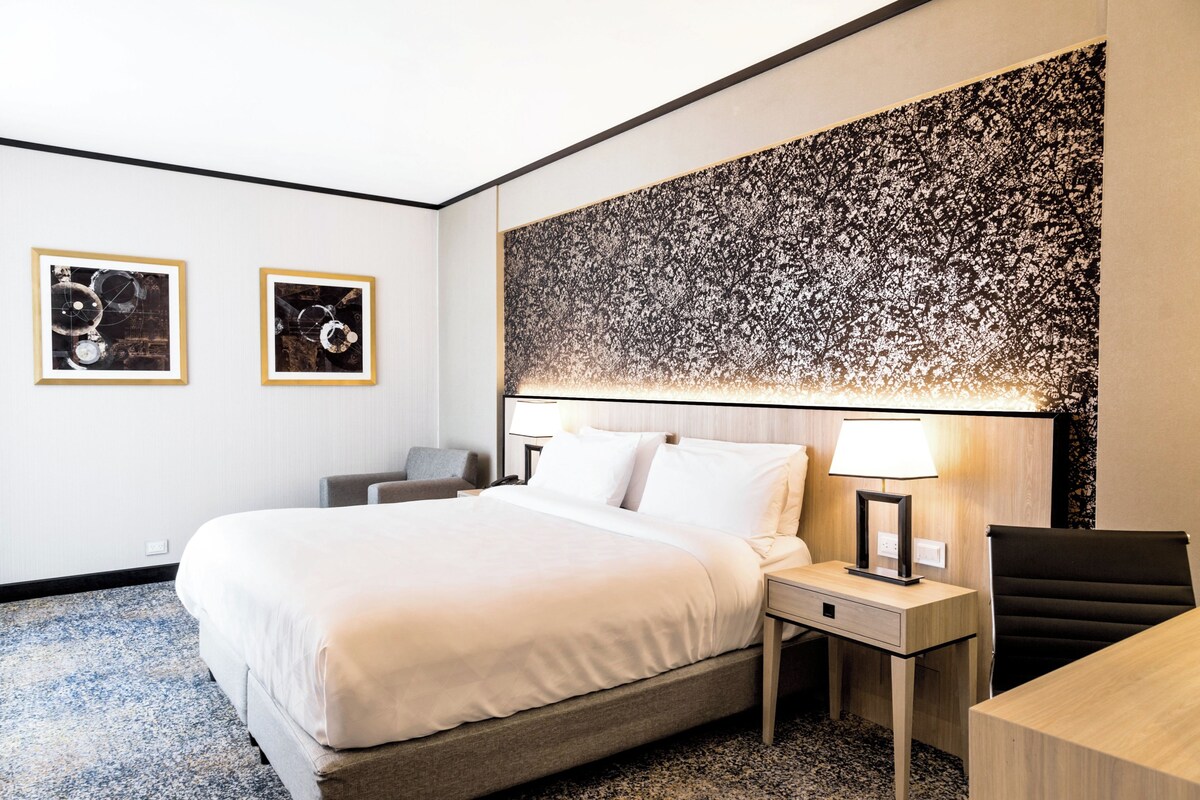 Een hotelkamer met een bed, nachtkastjes, een bureau en twee ingelijste foto's aan de muur.