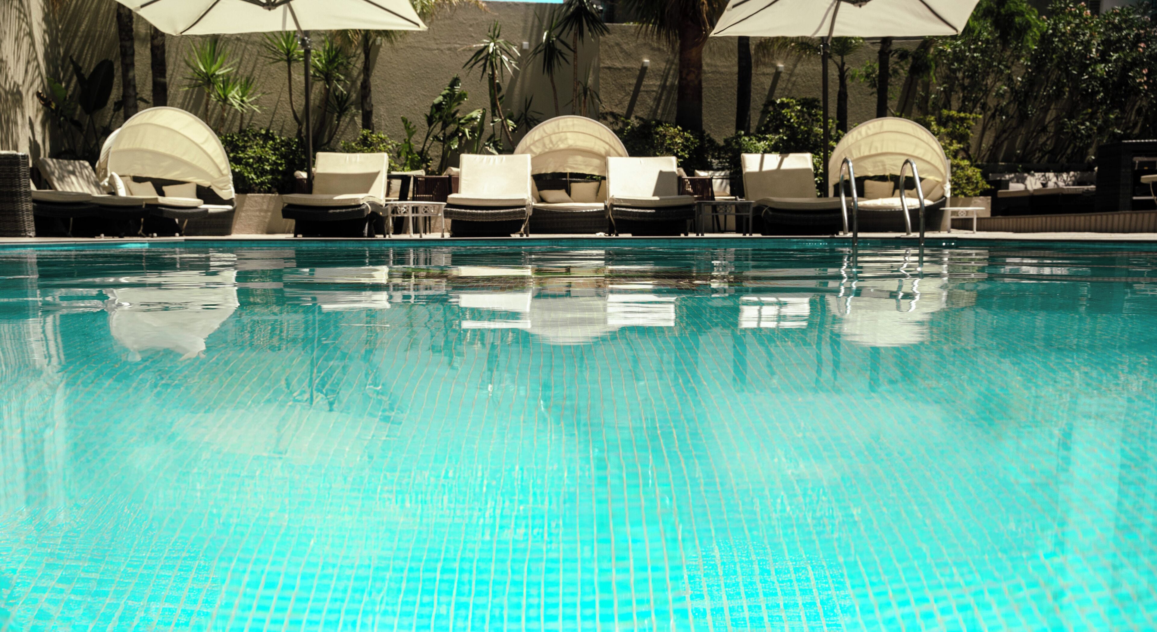 Una piscina con suelo de baldosas, rodeada de sillones de descanso y sombrillas.