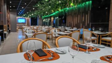 A restaurant with tables set for dining, featuring a modern interior with green foliage hanging from the ceiling and ambient lighting.