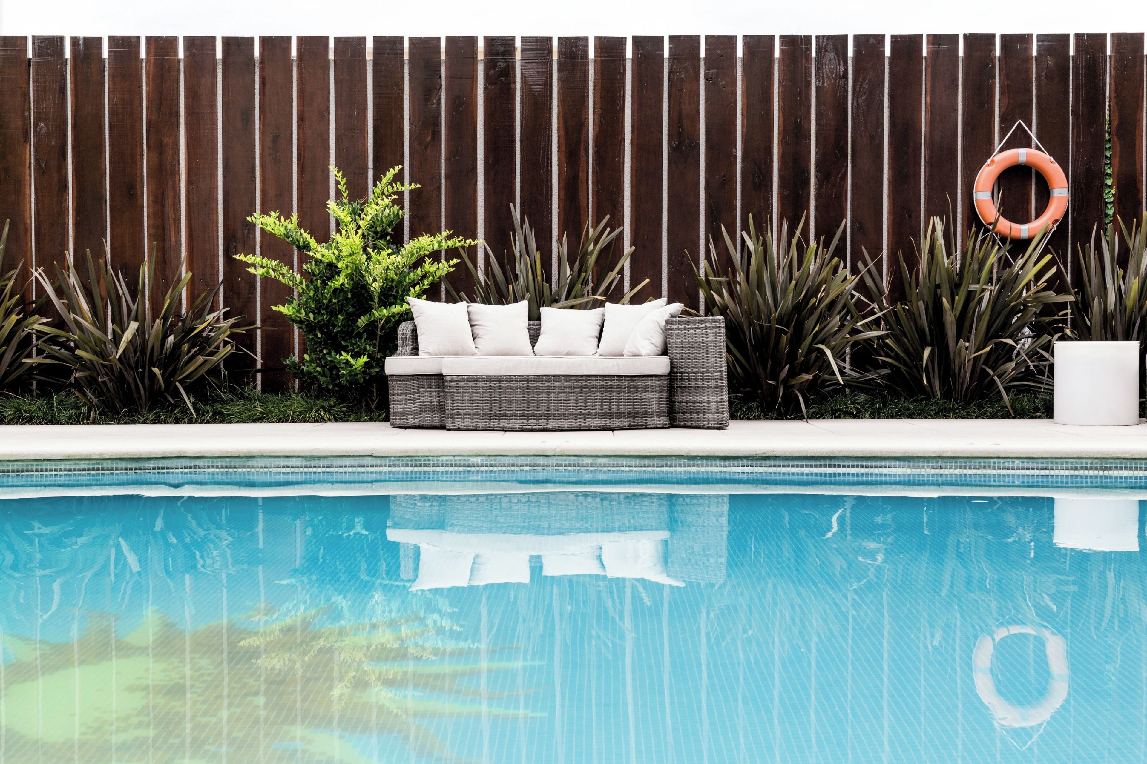 A poolside area with a wicker sofa, a life ring, and various plants.