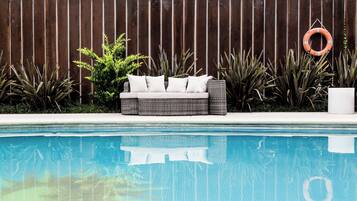Un área junto a la piscina con un sofá de mimbre, un flotador salvavidas y varias plantas.