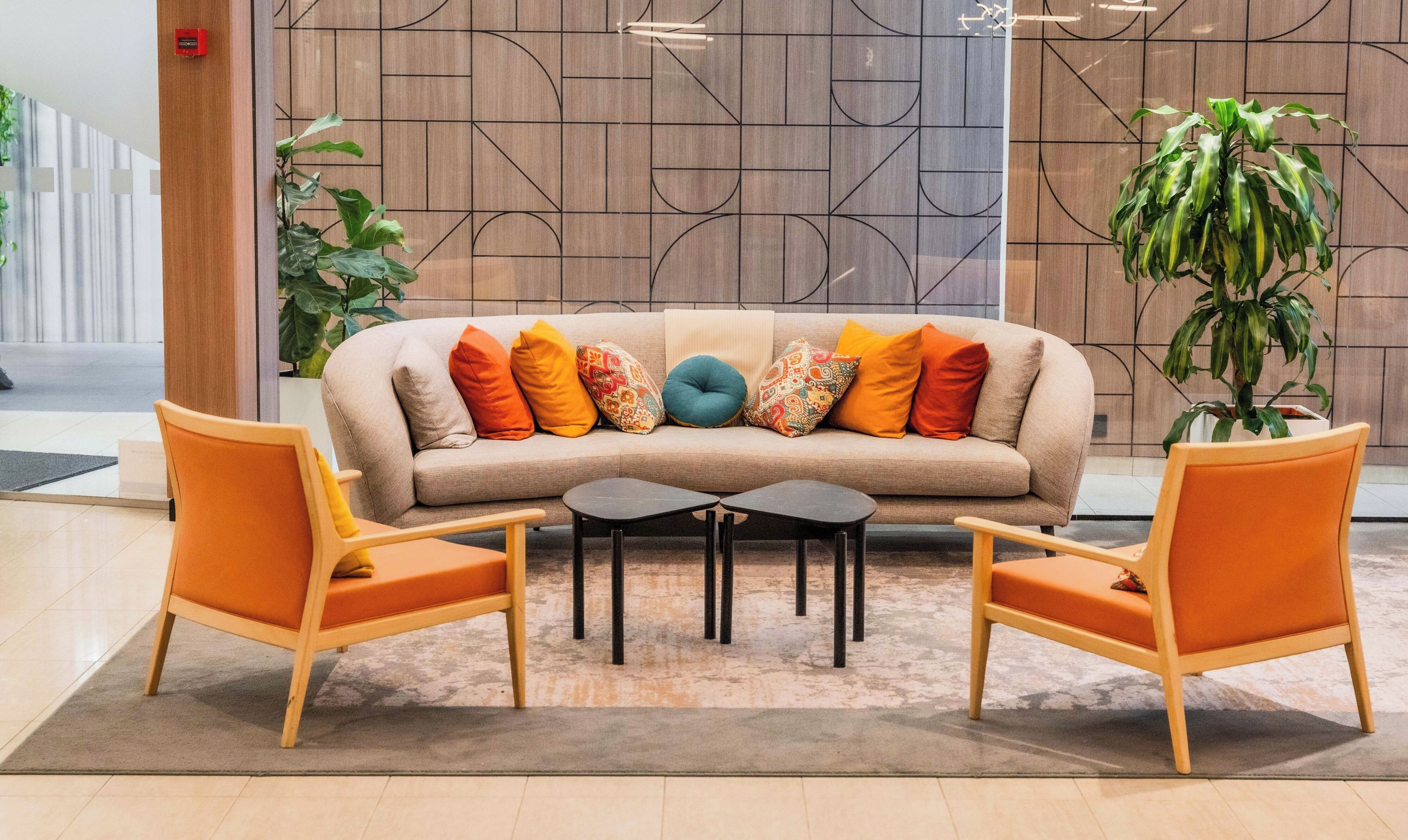 Un área de descanso moderna con un sofá color beige, cojines coloridos, dos sillones de madera y una mesita de centro.