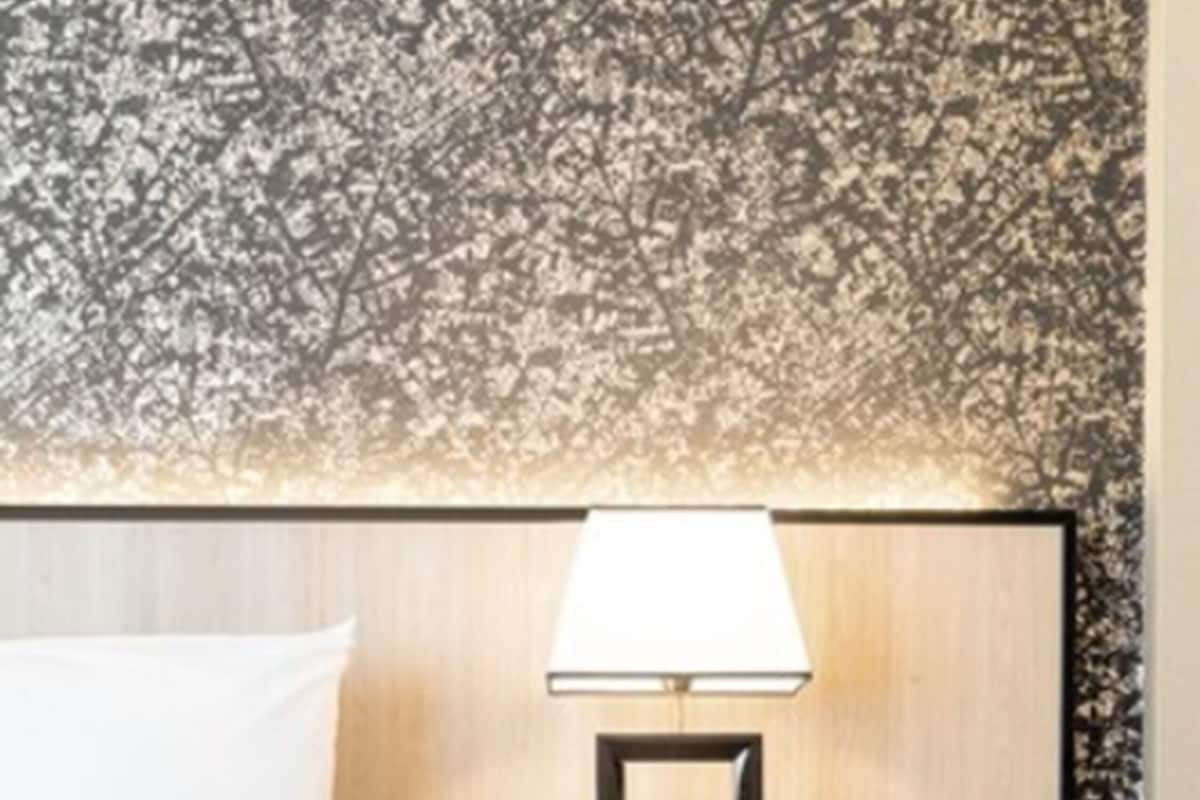 A hotel room with a bed, a nightstand with a lamp, and a patterned wall.