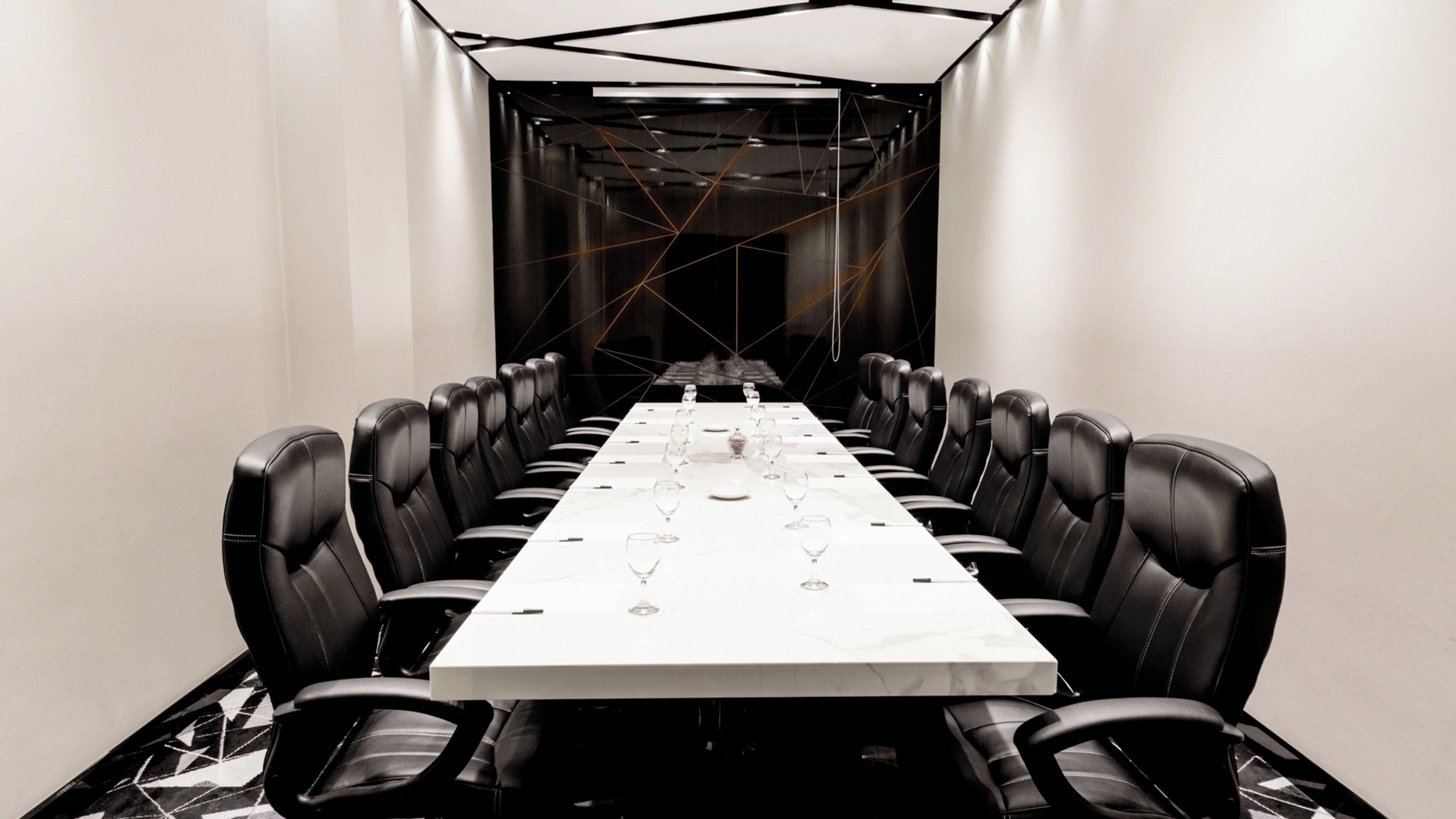 Ein Konferenzraum mit langem Tisch, schwarzen Ledersesseln und Weingläsern für eine Besprechung.