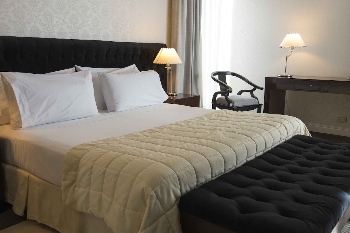 Une chambre d’hôtel avec un lit, deux lampes de chevet, une chaise et une table de chevet.