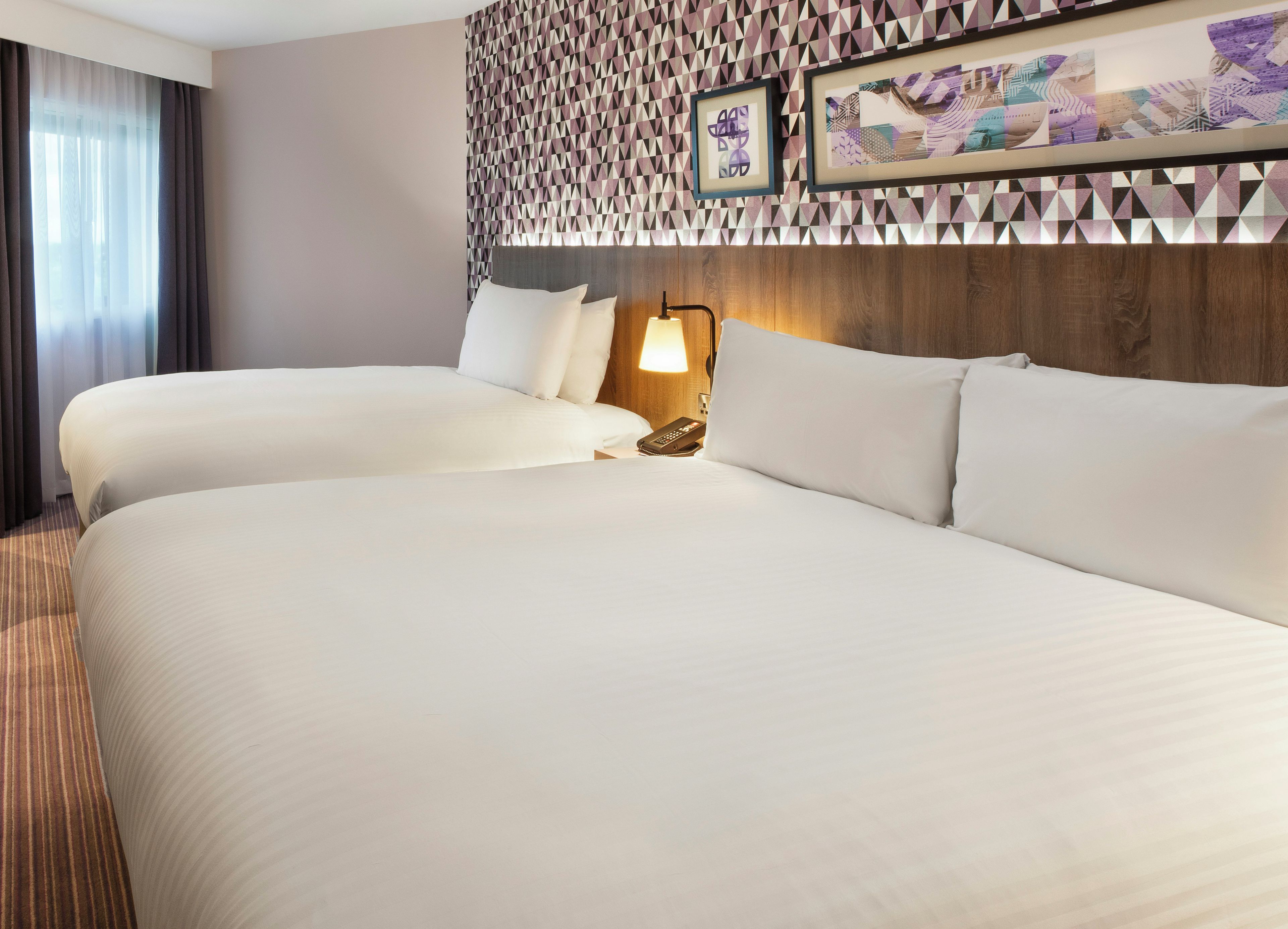 A hotel room with two beds, a wall-mounted lamp, and framed artwork.