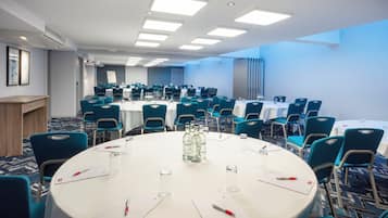 Un salón de conferencias con mesas redondas, sillas azules y manteles blancos.