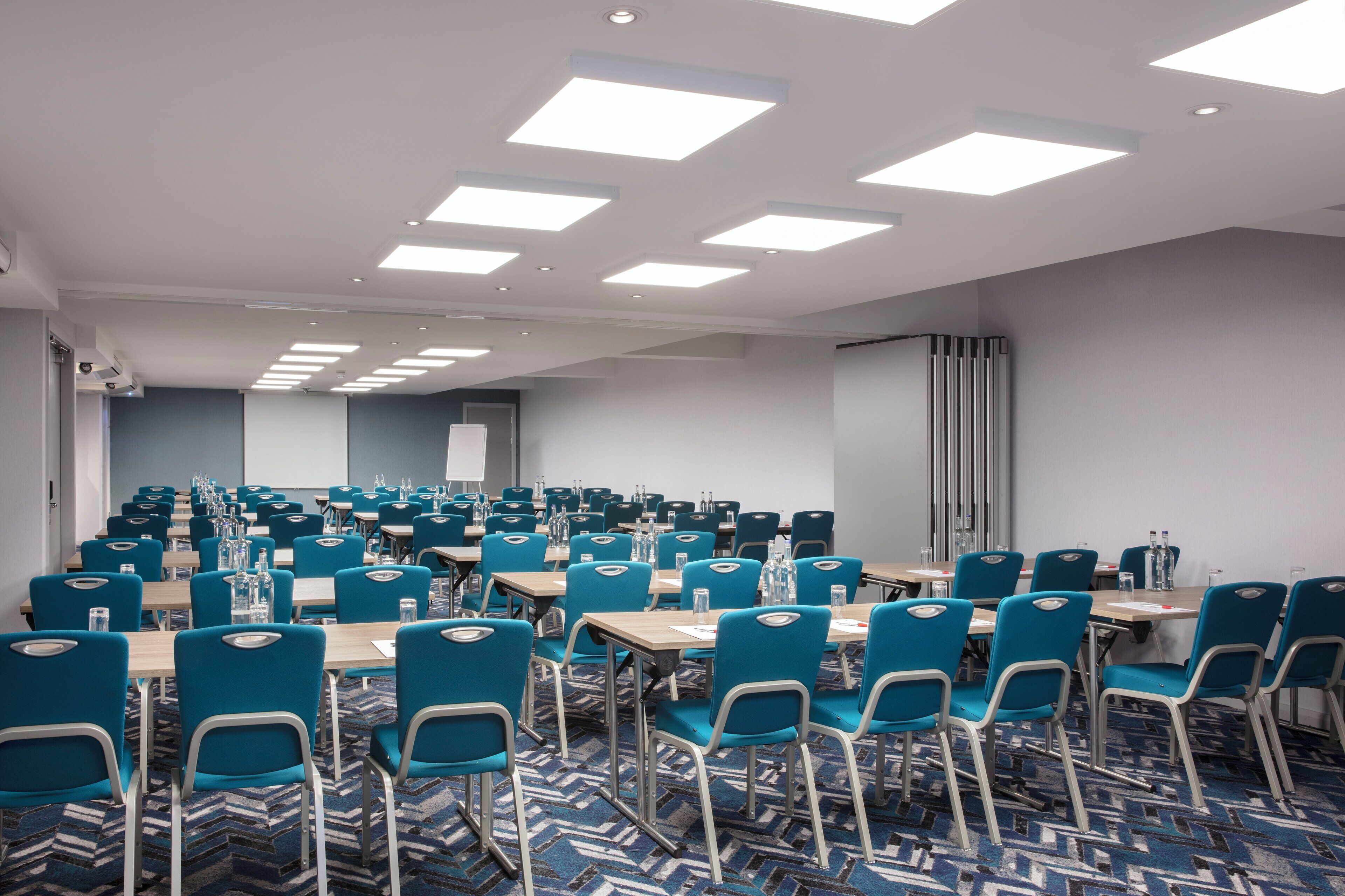 A conference room with rows of tables and chairs, equipped with water bottles and papers.