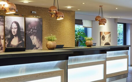 A reception desk with modern design, featuring a wooden finish, integrated lighting, and decorative elements like plants and artwork.