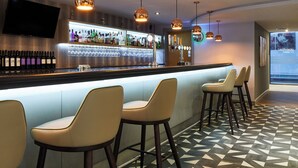 En bar med en lang disk, flere barstole og et udvalg af flasker og glas.