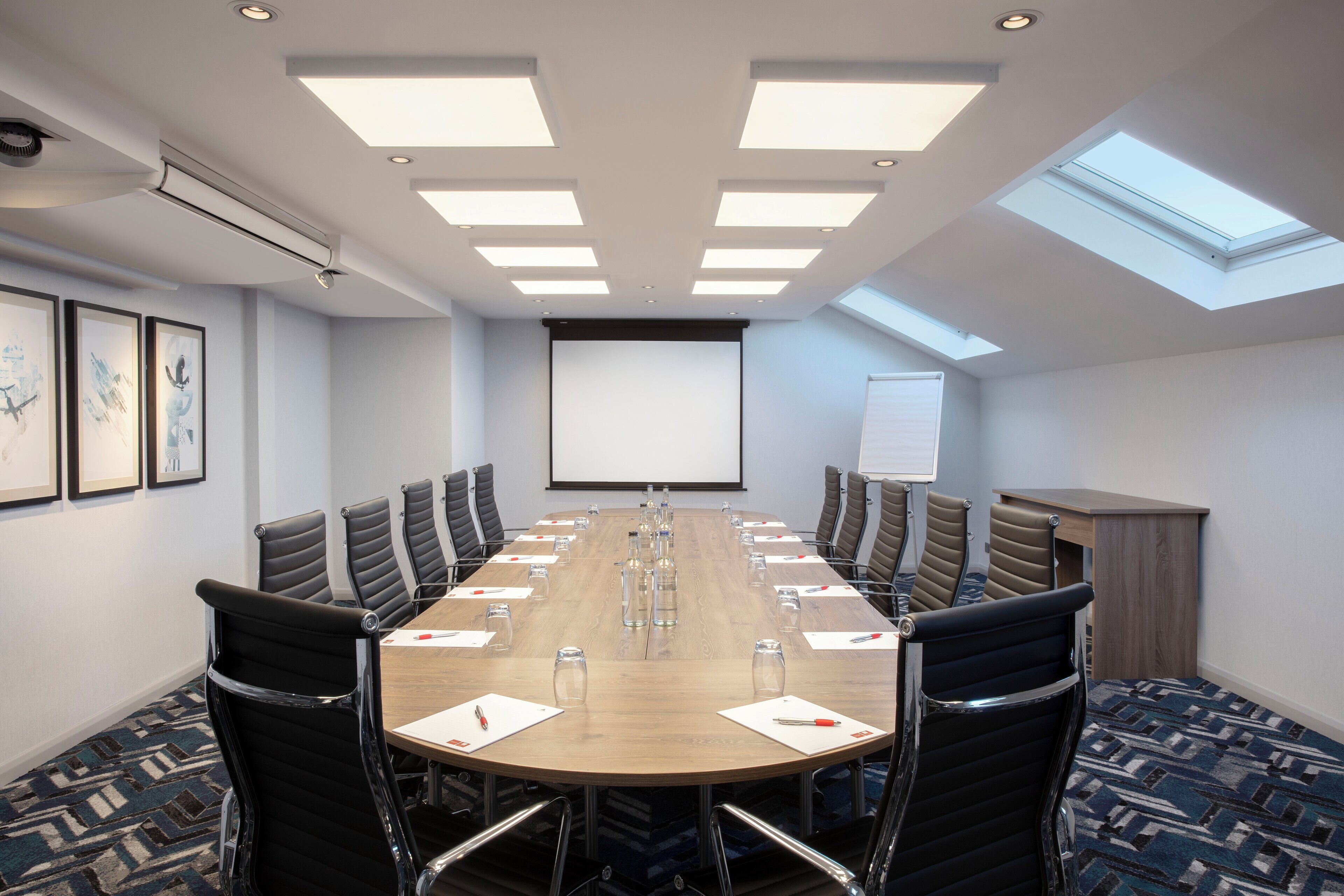 Une salle de conférence équipée d’une longue table, de chaises, d’un écran de projection et d’un tableau blanc.