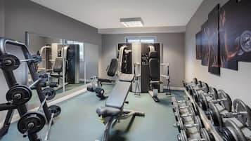 A gym with weightlifting equipment, a bench, and mirrors on the walls.