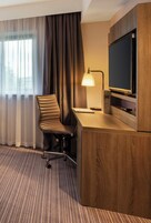 A hotel room with a wooden desk, a chair, a television, and a lamp.