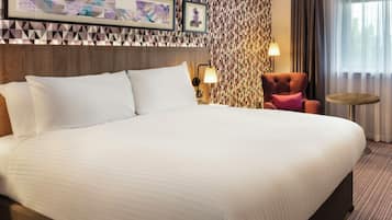 Habitación de hotel con una cama grande, una silla, una mesita y una pared con patrones geométricos.