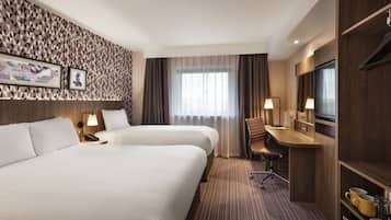 A hotel room with two beds, a desk, a chair, a TV, and a minibar.