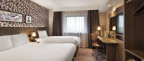 Een hotelkamer met twee bedden, een bureau, een stoel, een televisie en een minibar.