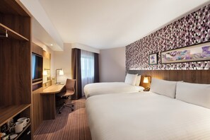 A hotel room with two beds, a desk, a chair, and a minibar. - Leonardo London Heathrow Airport (West Drayton)