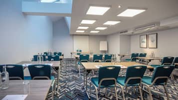 A conference room with a large table, teal chairs, and a patterned carpet.