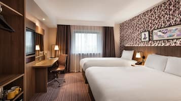 A hotel room with two beds, a desk, a chair, and a TV.