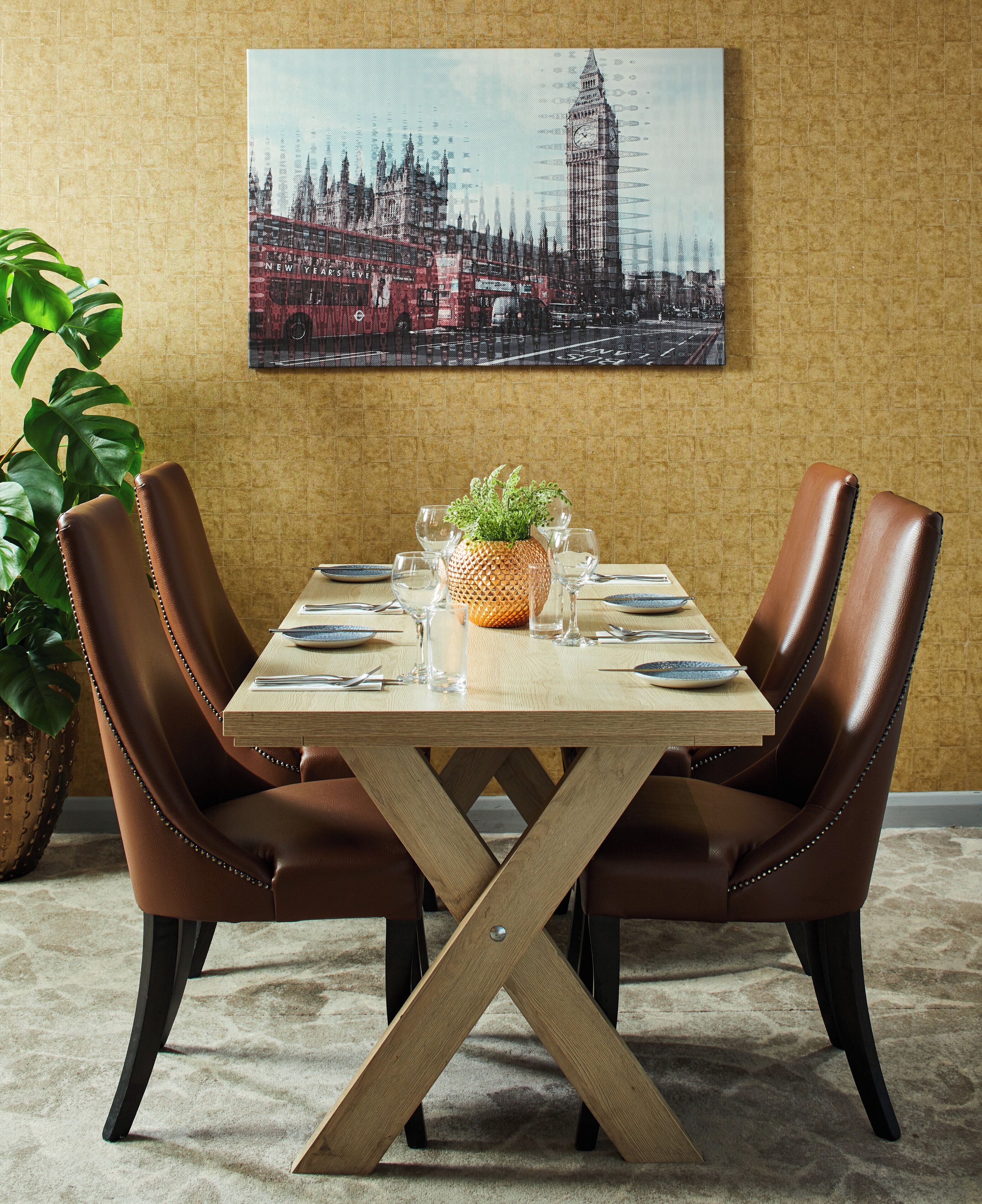 A dining table with a cross-braced wooden base, surrounded by leather chairs, set with plates, glasses, and a centerpiece.