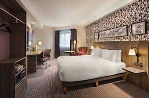 A hotel room with a large bed, a desk, a chair, and a small table.