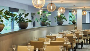 En restaurant med flere borde, stole og hængende pendellamper.