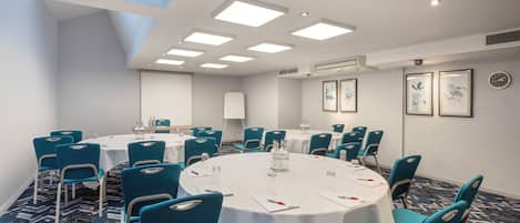 A conference room with round tables, teal chairs, and a patterned carpet.
