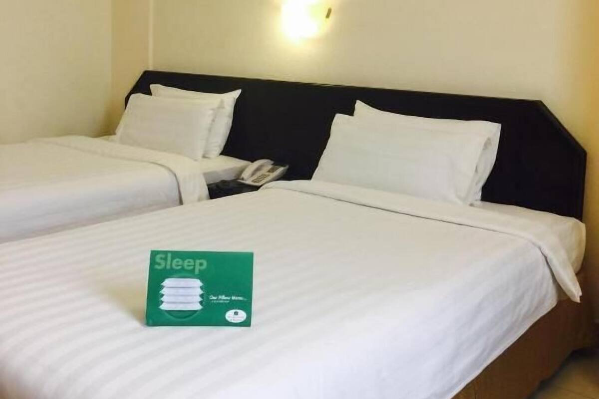 A hotel room with two beds, a framed picture on the wall, and a green sign on the bed.