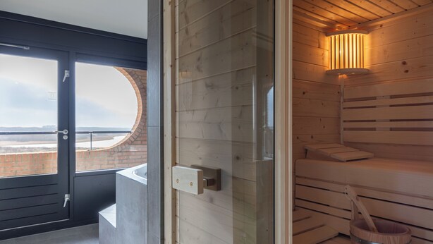 A sauna room with wooden benches, a glass door leading outside, and a wooden bucket with a ladle.