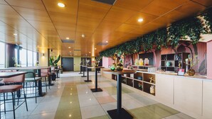 A modern cafe with multiple tables and chairs, a counter with a variety of items, and a ceiling with recessed lighting.
