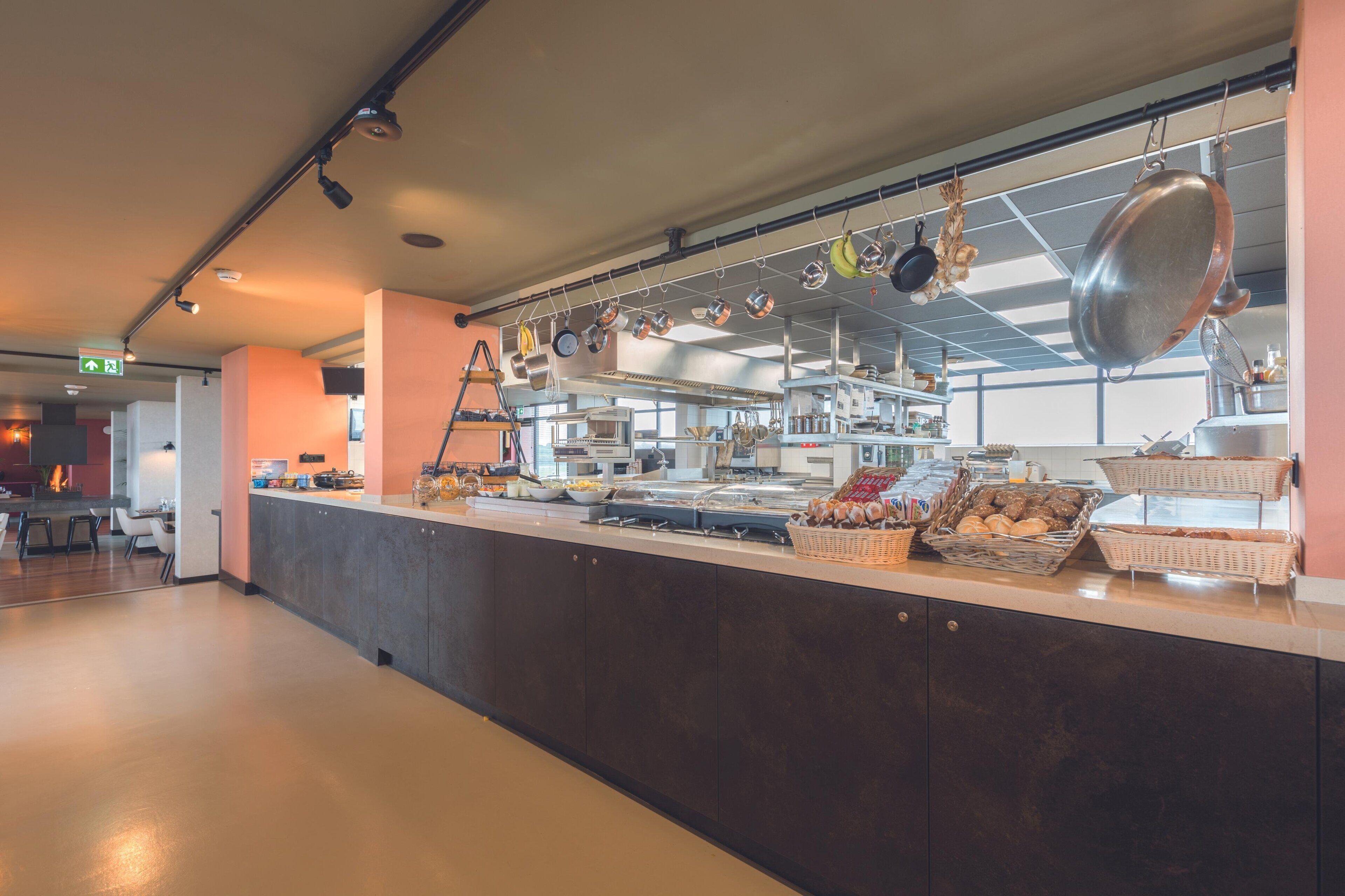 A modern kitchen with a long counter, hanging pots, and various food items displayed.