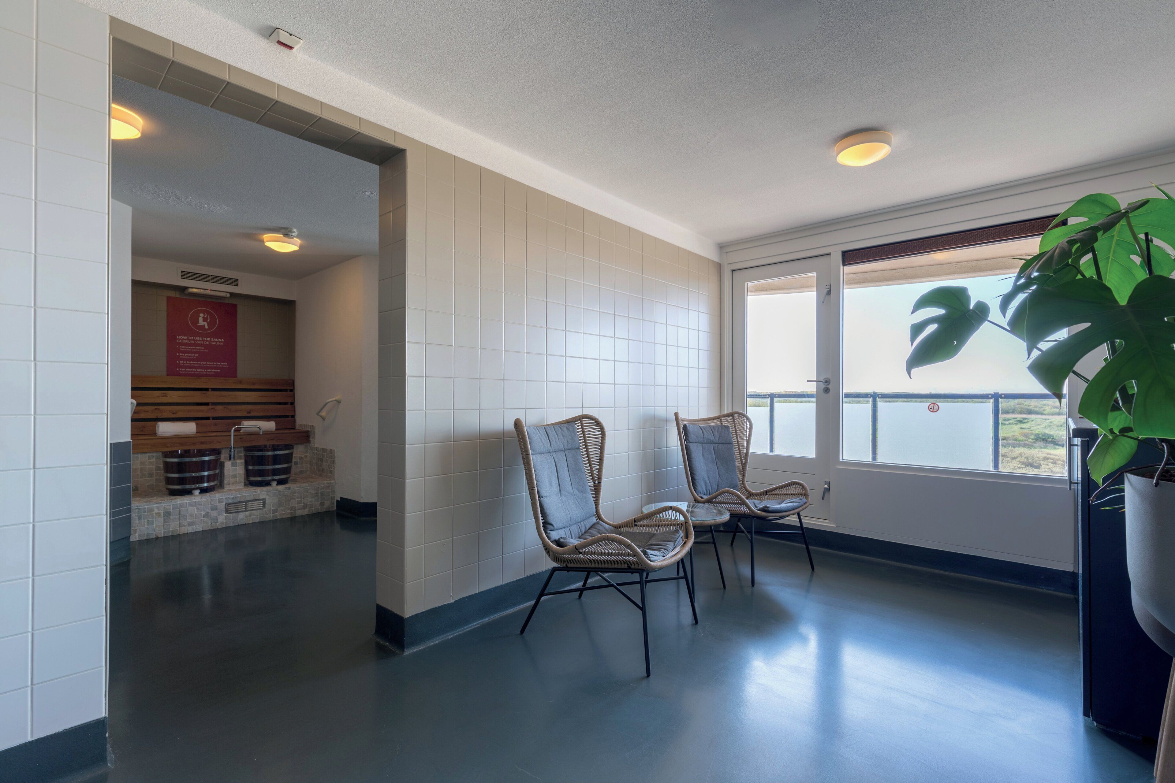 A hallway with two wicker chairs, a potted plant, and a view of the outdoors through a window.