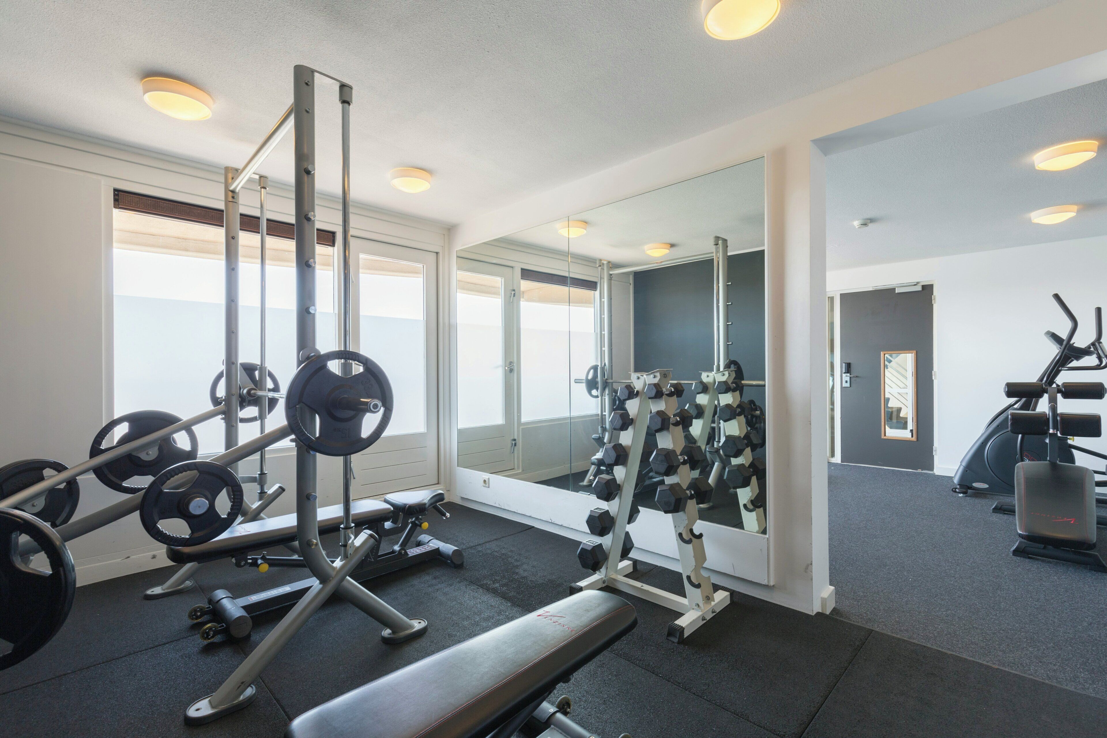 A gym with weightlifting equipment, a bench, and mirrors.