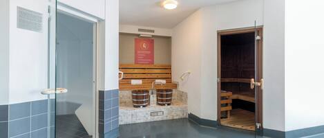 Un baño moderno con cabina de ducha de vidrio, un banco de madera y dos cubos de madera.