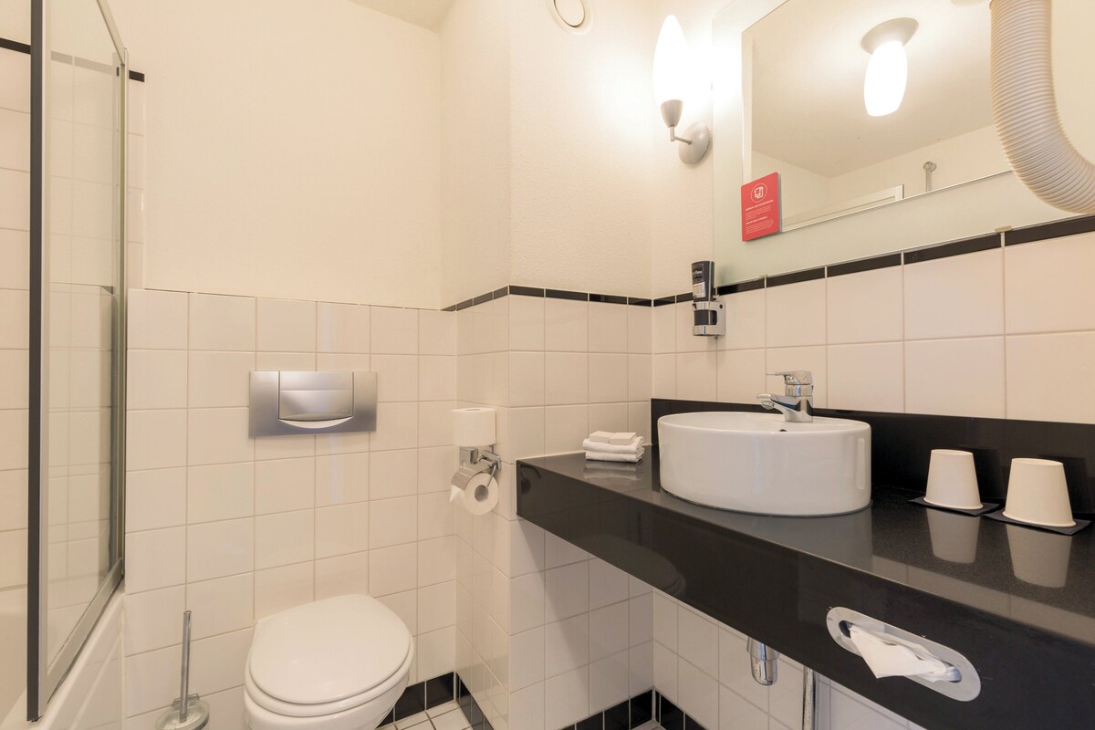 Un baño moderno con un inodoro blanco, una encimera negra con un lavabo y un espejo sobre el lavabo.