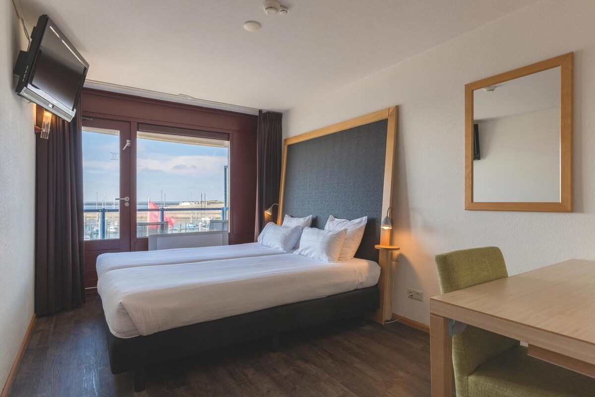 Une chambre d’hôtel équipée d’un lit, d’un bureau, d’une chaise, d’une télévision et offrant une vue sur l’extérieur.